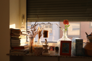 Auf einer Fensterbank: Bücher, Kerzenständer, Blume, Fotorahmen, alles in goldenes Licht getaucht