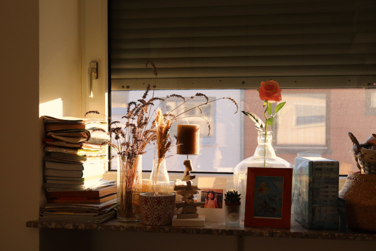 Auf einer Fensterbank: Bücher, Kerzenständer, Blume, Fotorahmen, alles in goldenes Licht getaucht